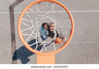 Happy father and teen daughter embracing and standing under a basketball hoop net, directly above