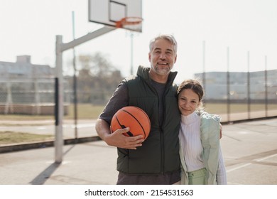 Happy Father And Teen Daughter Embracing And Looking At Camera Outside At Basketball Court.