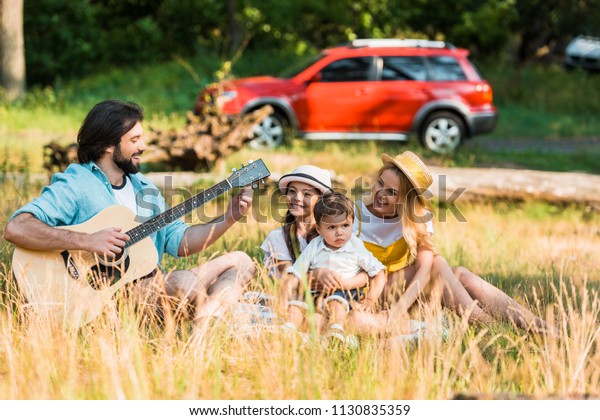 happy father\
tuning acoustic guitar at\
picnic