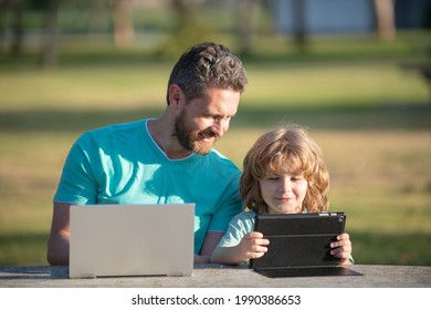 Happy Father Using Laptop Relax With Schooler Son Holding Laptop Have Fun Together, Smiling Dad And Little Boy Child Enjoy Weekend With Gadgets Outside On Nature.