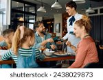 Happy father using mobile phone while paying to a waitress in restaurant at the hotel. 