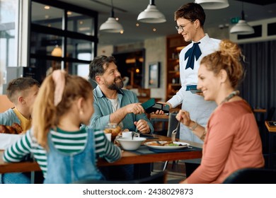 Happy father using mobile phone while paying to a waitress in restaurant at the hotel.  - Powered by Shutterstock