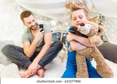 Happy father using smartphone while little son hugging with teddy bear - Powered by Shutterstock