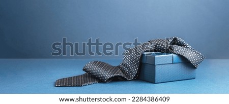 Happy Fathers Day background banner. Two blue gift boxes with ribbon bow and necktie on dark blue table. Monochrome. Gift delivery for him. Male fashion