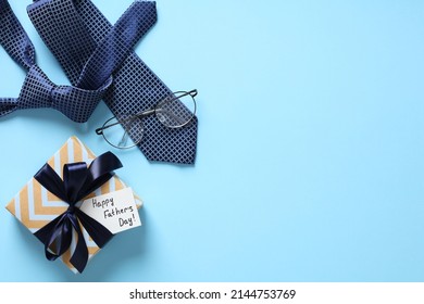 Happy Fathers Day background. Flat lay Happy Fathers Day gift box, necktie, glasses on pastel blue table.