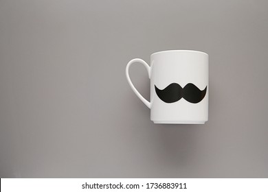 Happy Fathers Day, Boss Day Concept, White Tea Or Coffee Mug With Mustache On Grey Background, Copy Space.