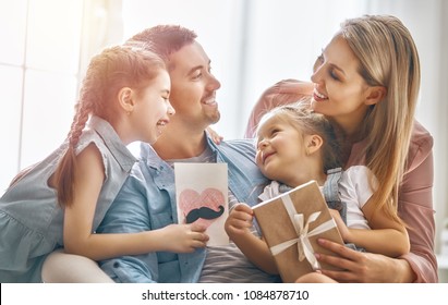 Happy father's day! Children daughters and their mom are congratulating dad and giving him postcard and gift box. Daddy and girls smiling and hugging. Family holiday and togetherness. - Powered by Shutterstock