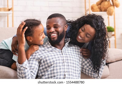 Happy Father's Day Concept. African American Man Enjoying Spending Time With Wife And Daughter At Home, Enbracing And Laughing Together
