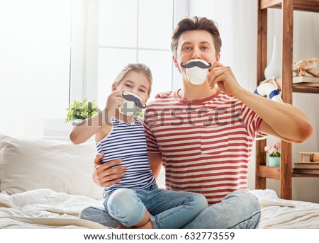 Happy father's day! Dad and his child daughter are playing and having fun together. Beautiful funny girl and daddy have mustaches on cups. Family holidays and togetherness.