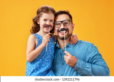 Happy Father's Day! Funny Dad And Daughter With Mustache Fooling Around On Colored Yellow Background
