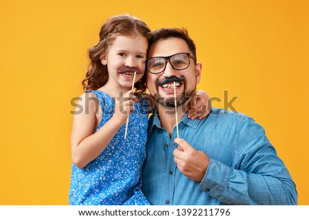 happy father's day! funny dad and daughter with mustache fooling around on colored yellow background
