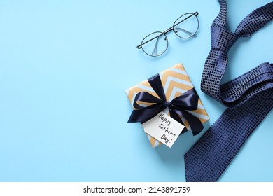 Happy Fathers Day gift box, necktie, glasses on pastel blue background. Flat lay, top view, copy space. - Shutterstock ID 2143891759