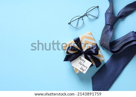 Happy Fathers Day gift box, necktie, glasses on pastel blue background. Flat lay, top view, copy space.