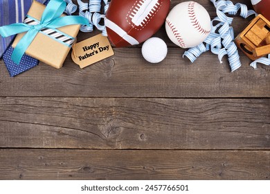 Happy Fathers Day gift tag with top border of gifts, ties, games and sport items. Overhead view on a rustic wood background. Copy space.