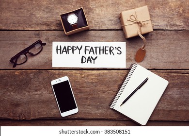 Happy Father's Day inscription with mobile phone, notebook, glasses and watch on wooden background. Greetings and presents - Powered by Shutterstock