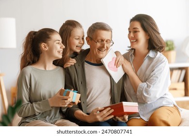 Happy father's day! Mother and daughter congratulating grandfather and giving him gift box. Family holiday and togetherness.