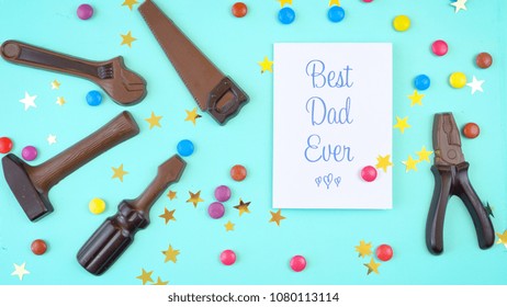 Happy Father's Day Overhead Of Chocolate Tool Set And Candy With Best Dad Ever Greeting Card On Pale Blue Aqua Table.