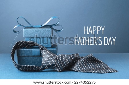 Happy Fathers Day text background banner. Two blue gift boxes with ribbon bow and necktie on dark blue table. Monochrome. Gift delivery for him. Male fashion. Greeting card