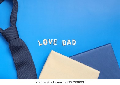 Happy Father's Day. Word LOVE DAD made with wooden letters, tie and gift boxs on blue background, flat lay. Space for text - Powered by Shutterstock