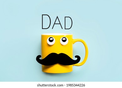 Happy Father's Day.Yellow mug with mustache and funny eyes looking up with the text Dad on a blue background