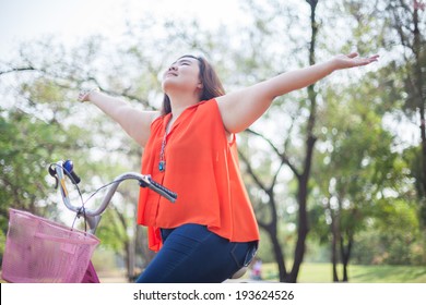 Happy fatty asian woman outstretched with bicycle outdoor in a park