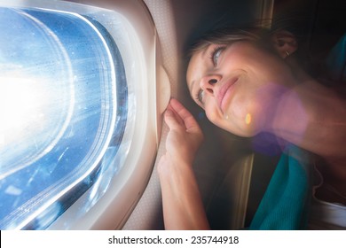 Happy, female airplane passanger enjoying the view from the cabin window over the blue sky (shallow DOF; intentional flare)