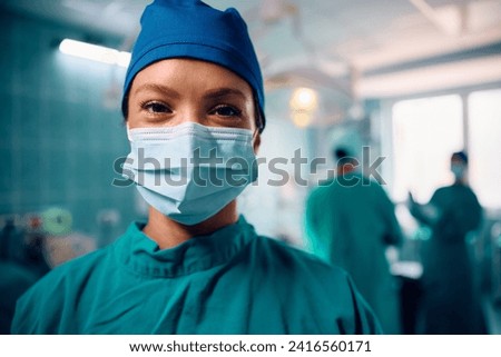 Happy female anesthesiologist during the surgery in operating room looking at camera. 