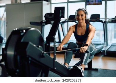 Happy female athlete having sports training on rowing machine in health club. Copy space. - Powered by Shutterstock