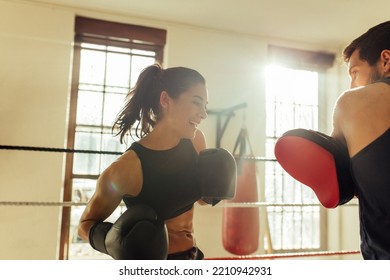 Happy Female Boxer Sparring With Instructor In Boxing Gym Besides Two Large Windows