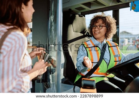 Happy female bus driver talking to a woman who is entering in vehicle at the station.