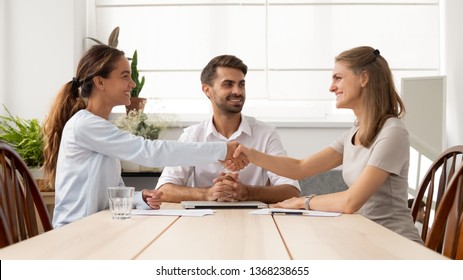 Happy female business partners shake hands sign two contracts with lawyer mediation at meeting, smiling businesswomen handshake make legal partnership deal after successful negotiations with mediator