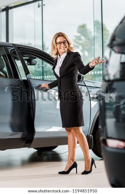 happy female\
car dealer opening car in\
showroom