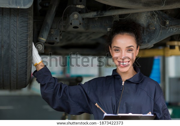 Happy female car mechanic worker working\
underneath lifted car. Female mechanic vehicle service maintenance\
checking under car condition in garage. Auto car repair service and\
maintenance concept