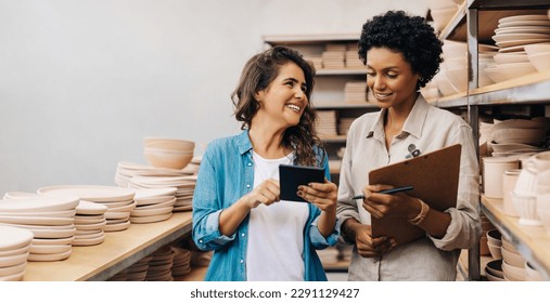 Happy female ceramists using a digital tablet together in their store. Business women managing a store with handmade ceramic products. Female entrepreneurs running a creative small business. - Powered by Shutterstock