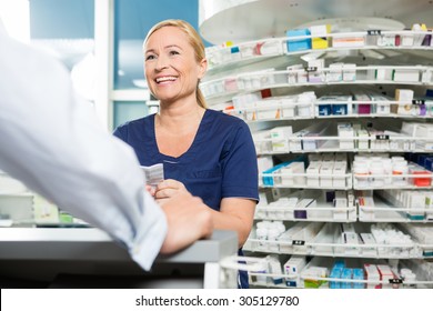 Happy Female Chemist Looking At Male Customer In Pharmacy