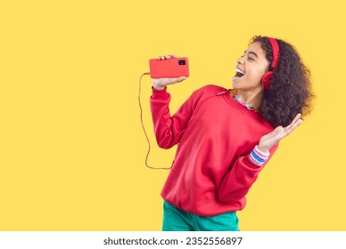 Happy female child singer listening to pop music on mobile phone. Side profile view joyful cheerful beautiful Afro American girl isolated on yellow background singing along with popular track playlist - Powered by Shutterstock