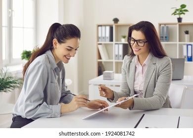 Happy female client signs a lease or purchase agreement given to her by a bank manager or real estate agent. Before signing the woman reads the terms of the mortgage, lease or purchase agreement.