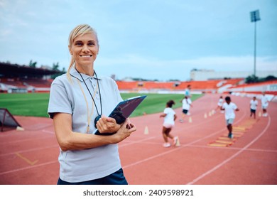 Happy female coach during PE class at athletics club looking at camera. The children are in the background. - Powered by Shutterstock