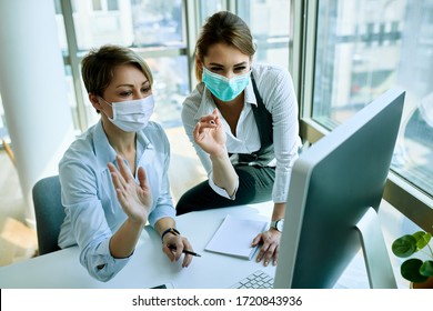 Happy female colleagues using computer and waving while making video call from the office during virus epidemic.  - Powered by Shutterstock