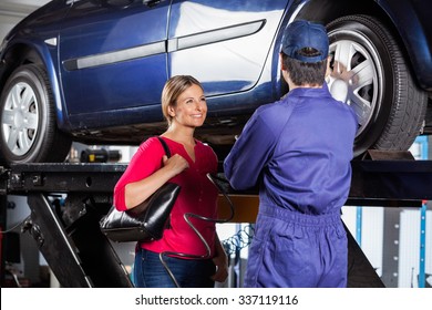 Happy Female Customer Looking At Mechanic Refilling Car Tire At Garage