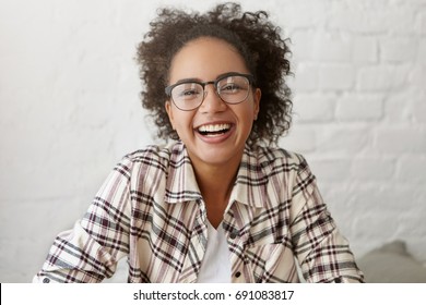 Happy female with dark pure skin and crisped hair wearing elegant glasses and shirt smiling sincerely into camera. Mixed race cute female student being glad to pass all her exams successfully