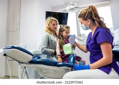 A happy female dentist checks the patient's teeth while her mother supports her in the office of the dental clinic. Dentistry technology technology and healthcare concept - Powered by Shutterstock