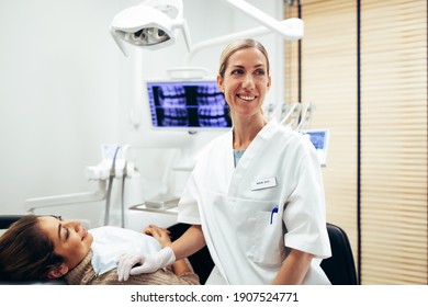 Happy Female Dentist Looking Away At Something With A Woman Patient Sitting On Dentist's Chair. Happy Dentist And Patient At Dental Clinic.