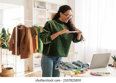 Happy Female Designer Or Fashion Blogger Taking Photo Of Garment On Phone Working In Modern Showroom Indoors. Fashion Entrepreneurship And Blogging, Design And Technology Concept