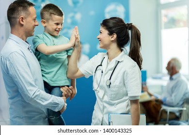 Happy female doctor giving high five to a little boy who came with father at hospital. 