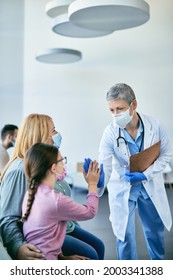 Happy Female Doctor And Little Girl Greeting With High-five Gesture In Waiting Room At The Hospital. They Are Wearing Face Masks Due To COVID-19 Pandemic.