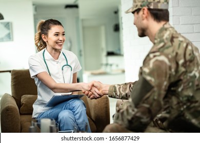 Happy Female Doctor And Military Man Shaking Hands While Meeting At His Home. 