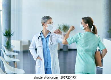 Happy Female Doctor And Nurse Greeting With Elbow And Wearing Face Masks At Medical Clinic During Coronavirus Pandemic.