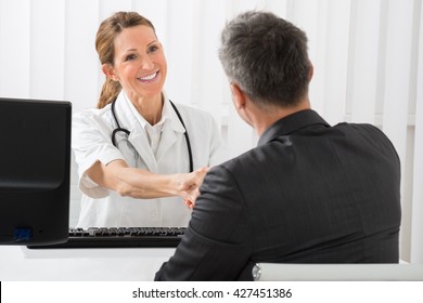 Happy Female Doctor Shaking Hands With Businessman In Hospital