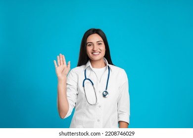 Happy Female Doctor Waving To Say Hello On Light Blue Background